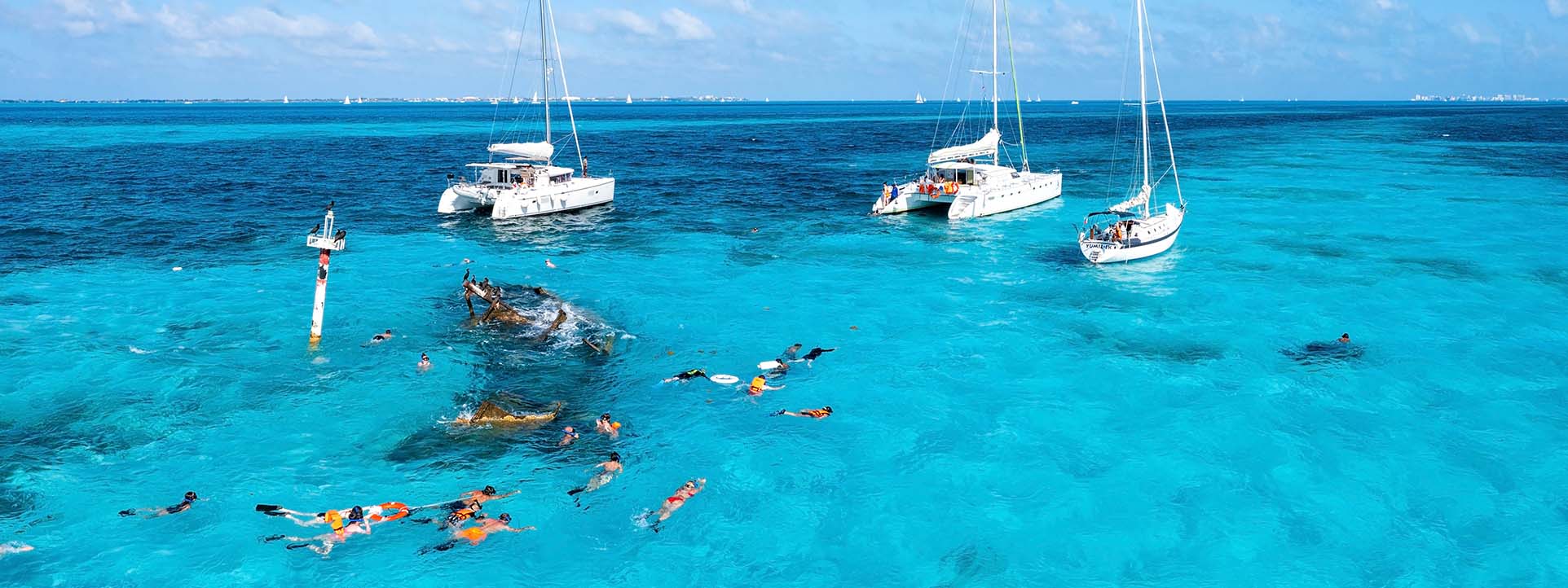 Schnorcheln vor der Küste auf einer Karibik Kreuzfahrt mit kristallklarem Wasser, Katamaranen und bunten Fischen